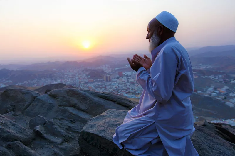 Pellegrino anziano in carrozzina accompagnato da un familiare in uno spazio pedonale della Mecca