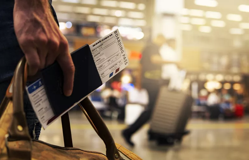 Passaporto italiano e smartphone accanto a una valigia, con un aeroporto sullo sfondo